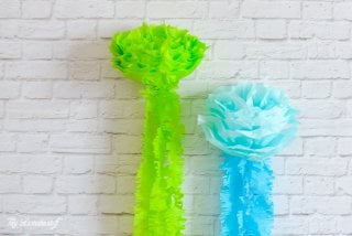 Green and blue tissue paper hanging on a white brick wall.  The tissue paper resembles jellyfish