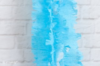 Fringed cut blue crepe paper hanging on a white brick wall