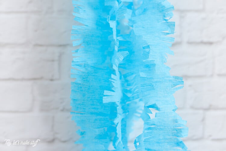 Fringed cut blue crepe paper hanging on a white brick wall