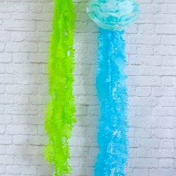 Green and blue tissue paper hanging on a white brick wall.  The tissue paper resembles jellyfish