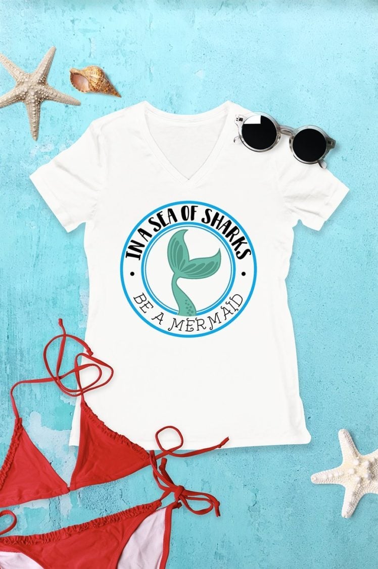 Seashells, a red bikini, sunglasses and a white t-shirt that has the saying, \"In a Sea of Sharks, Be a Mermaid\"
