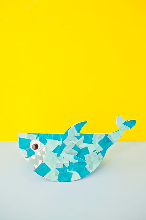 A shark image cut out of paper that has different shades of blue tissue paper glued to it and a googly eye