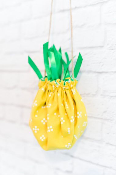 A cinched pineapple purse hanging on a white bricked wall