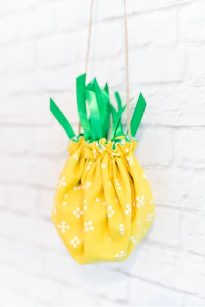 A cinched pineapple purse hanging on a white bricked wall