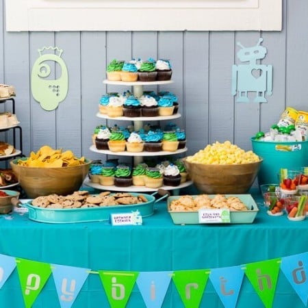 Buffet table set up with party food and cupcakes with a banner across the front of the table that says, "Happy Birthday"