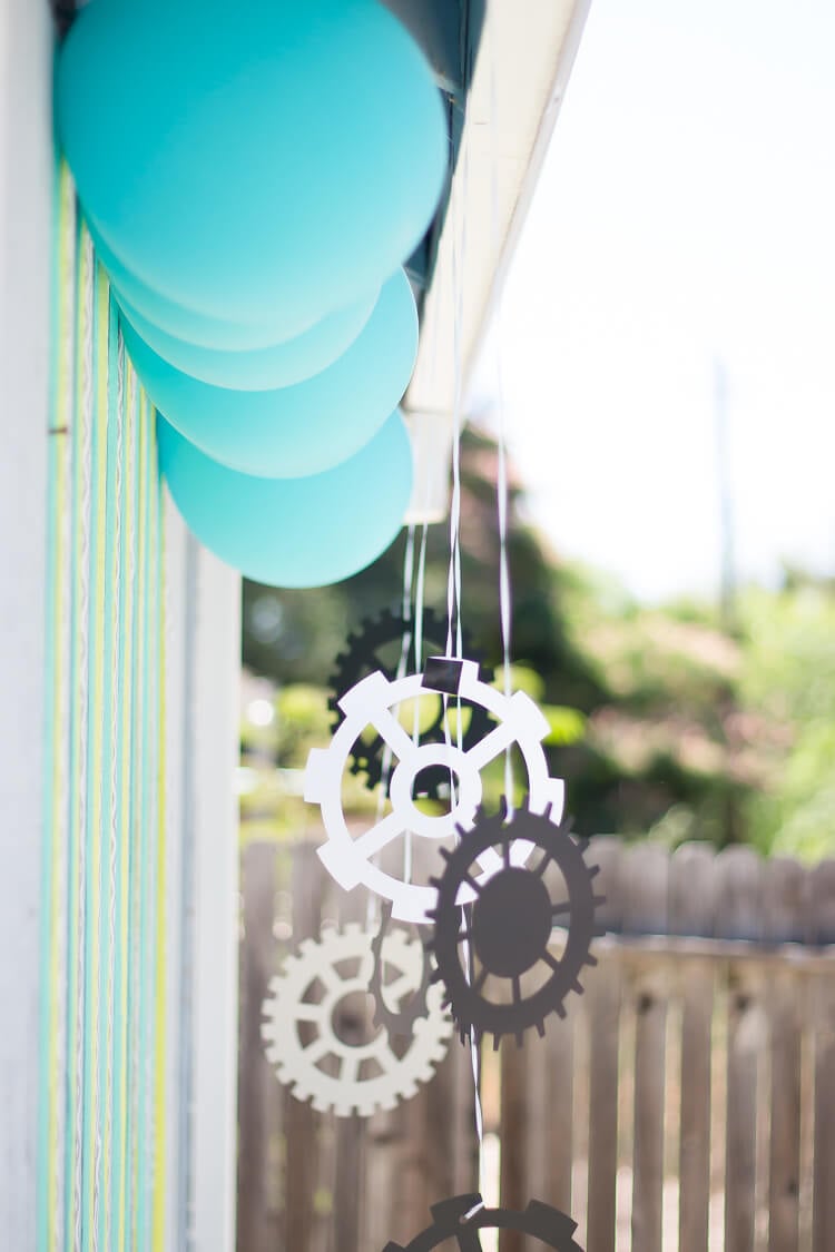 A close up of blue balloons and paper cut out gears hanging outside