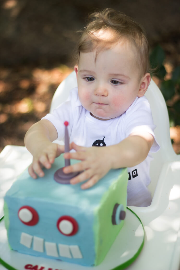 A little boy sitting in a highchair and playing with a robot cake