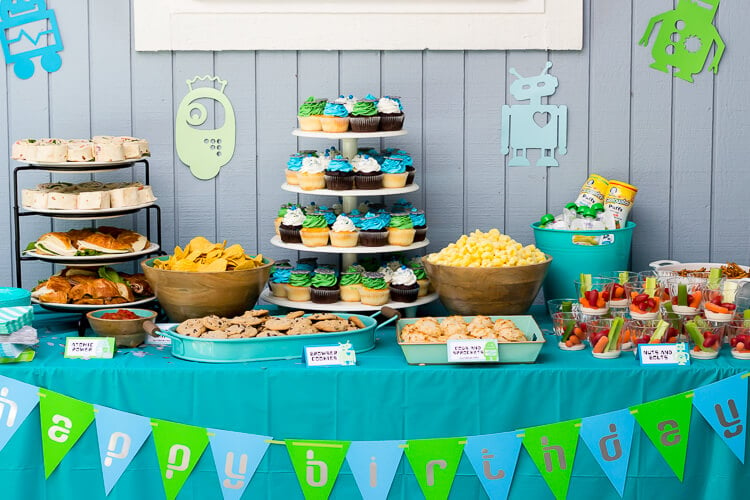 Buffet table set up with party food and cupcakes with a banner across the front of the table that says, \"Happy Birthday\"