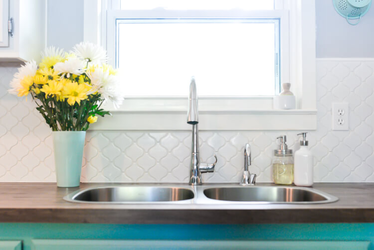 A vase of flowers on a kitchen counter next to a stainless-steel kitchen sink