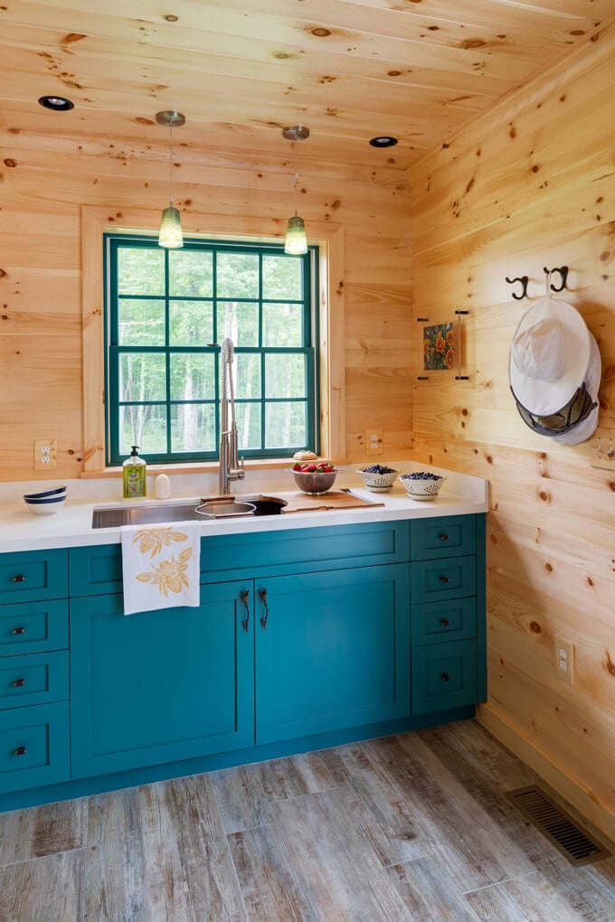 A kitchen with wooden walls, teal-colored cabinets and a wood floor