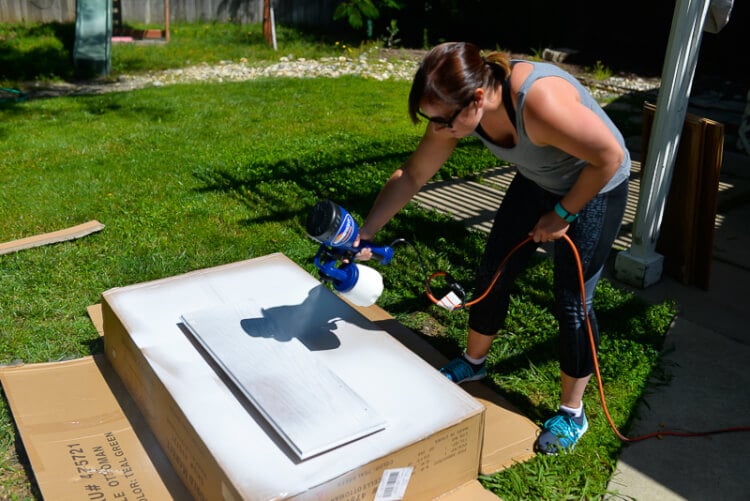 woman painting kitchen cabinets using a sprayer