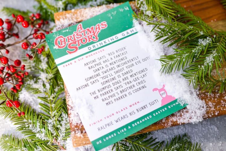 A piece of paper that contains a printed image of A Christmas Story Drinking Game laying on top of a table with holiday greenery on it