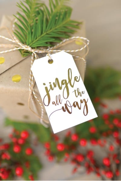 A package with a tag on it that says, "Jingle all the Way" and is sitting on top of a table decorated with holiday greenery and red berries