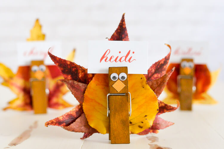 Close up of a place card holder made to look like a turkey using leaves from a tree and clothespins and personalized with a name