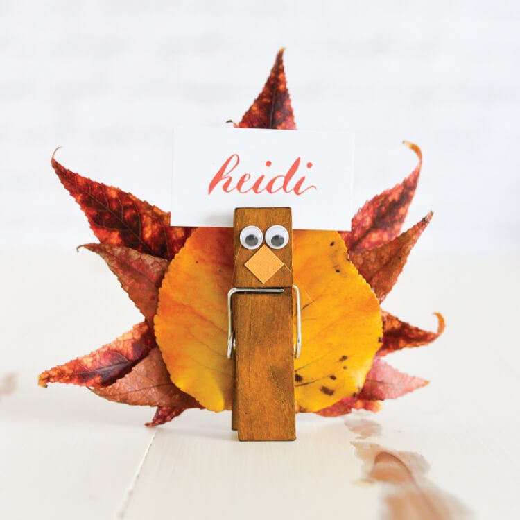 Close up of a place card holder made to look like a turkey using leaves from a tree and clothespins and personalized with a name