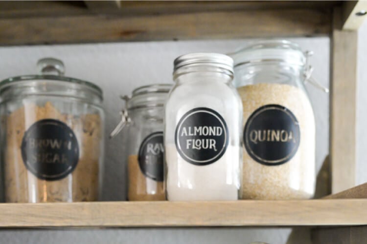 Jars sitting on a pantry shelf filled with food staples and labeled according to their contents