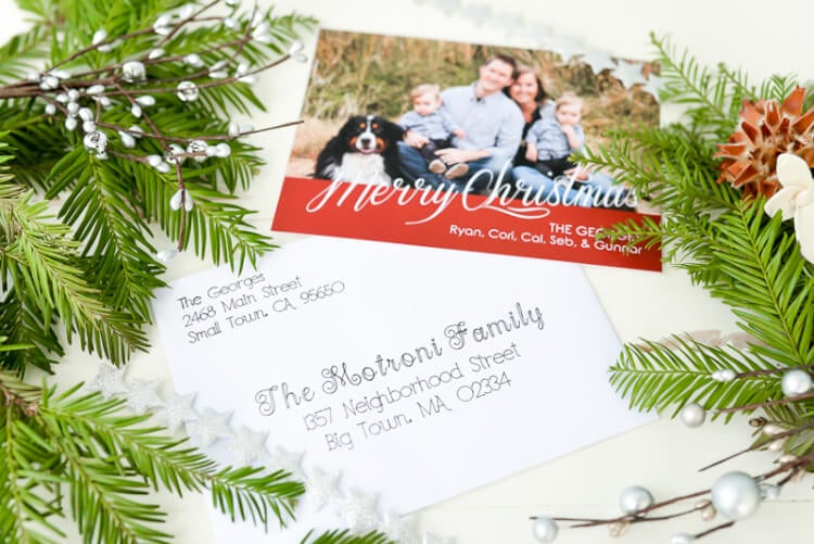 A Christmas card and an addressed envelope sitting next to some holiday greenery on a table