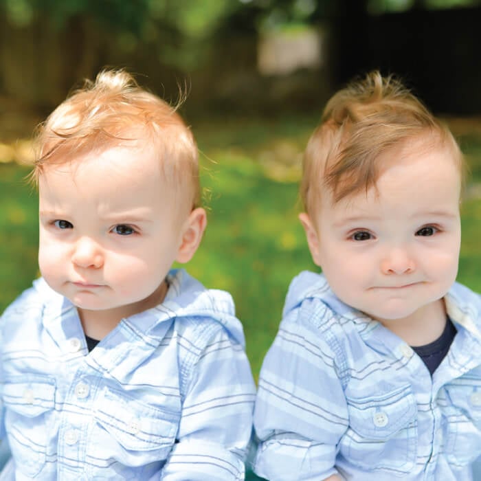 Two little boys sitting outside and dressed in blue and white striped shirts
