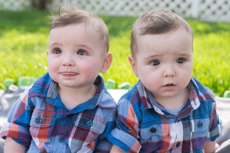 Two adorable little boys sitting outside, dressed in blue jeans and plaid shirts