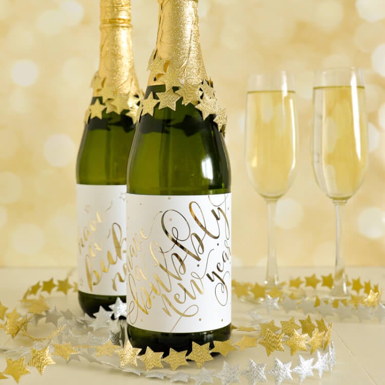 Two bottles of champagne and two champagne flutes sitting on a table surrounded by garlands of silver and gold stars