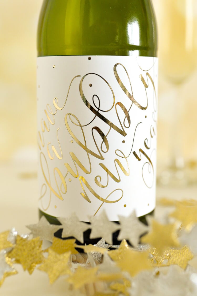 A close up of a bottle of champagne with a label on it that says, \"Have a Bubbly New Year\", sitting on a table surrounded by garlands of silver and gold stars
