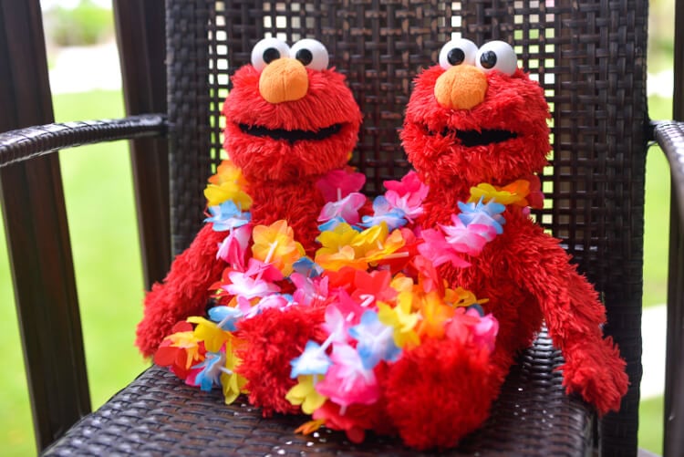 Two Elmo\'s wearing lei\'s and sitting on a lawn chair