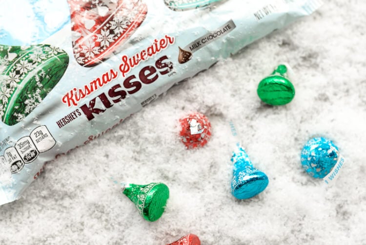 A package of Hershey\'s Kissmas Sweater Kisses next to more Hershey\'s kisses, all sitting on a table 