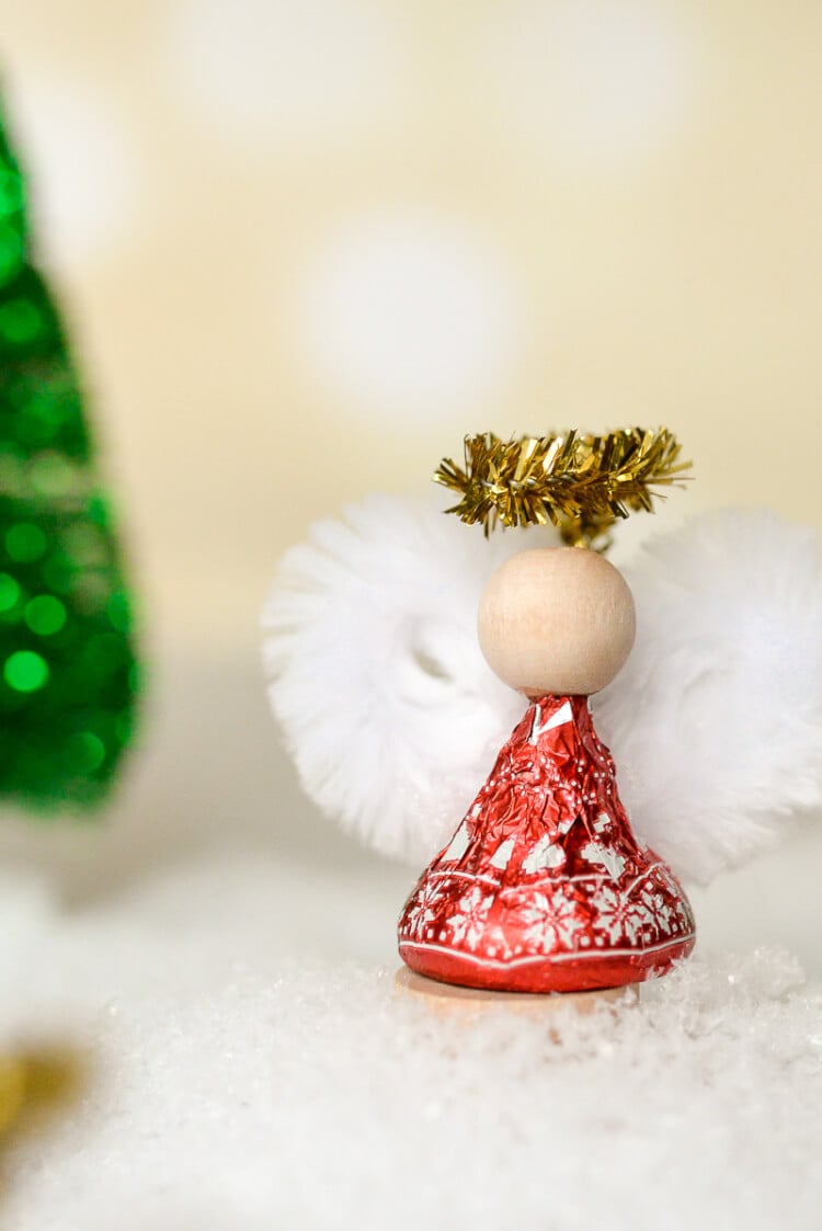 A red wrapped Hershey\'s kiss decorated to look like an angel using a wooden bead and white and gold chenille stems