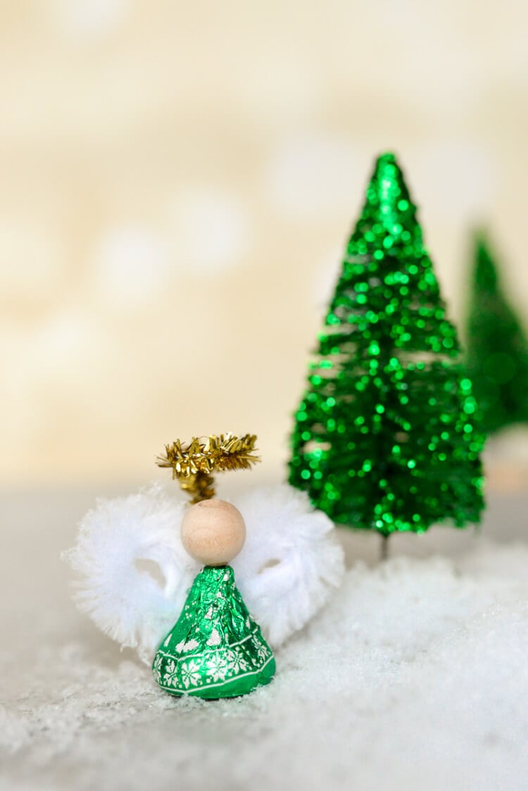 A green wrapped Hershey\'s kiss decorated to look like an angel using a wooden bead and white and gold chenille stems