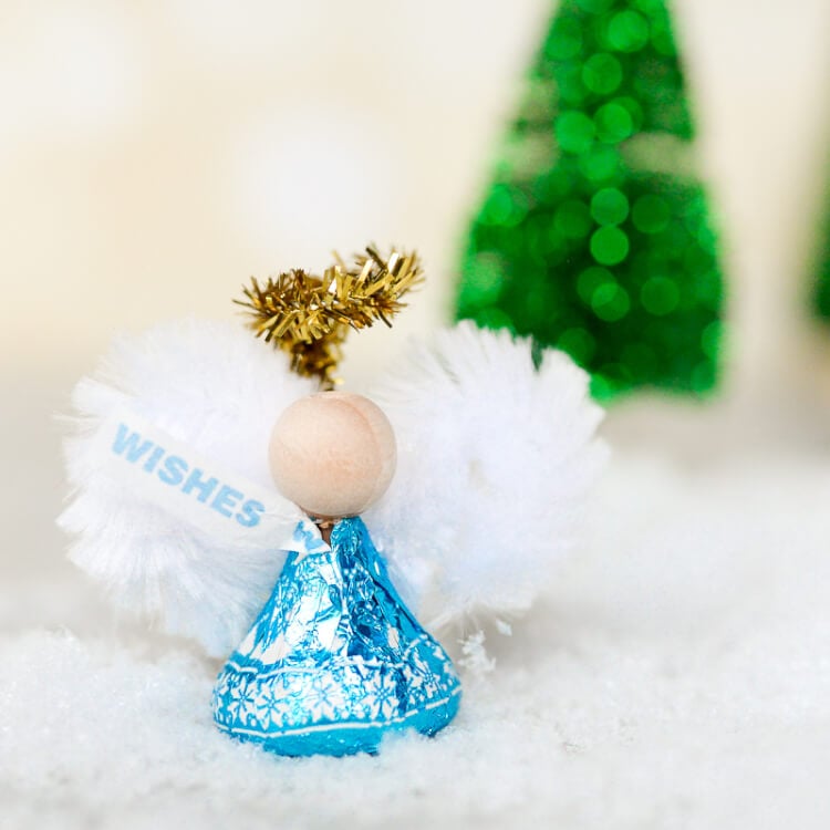 A blue wrapped Hershey\'s kiss decorated to look like an angel using a wooden bead and white and gold chenille stems