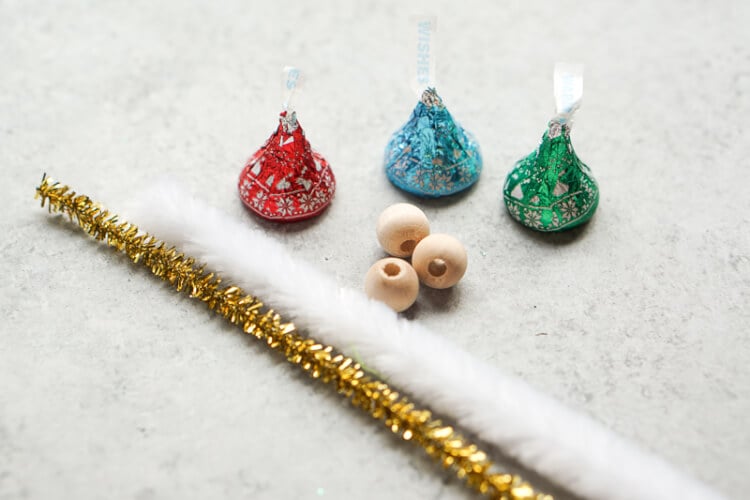 Hershey\'s Kisses, wooden beads and white and gold chenille stems laying on a table