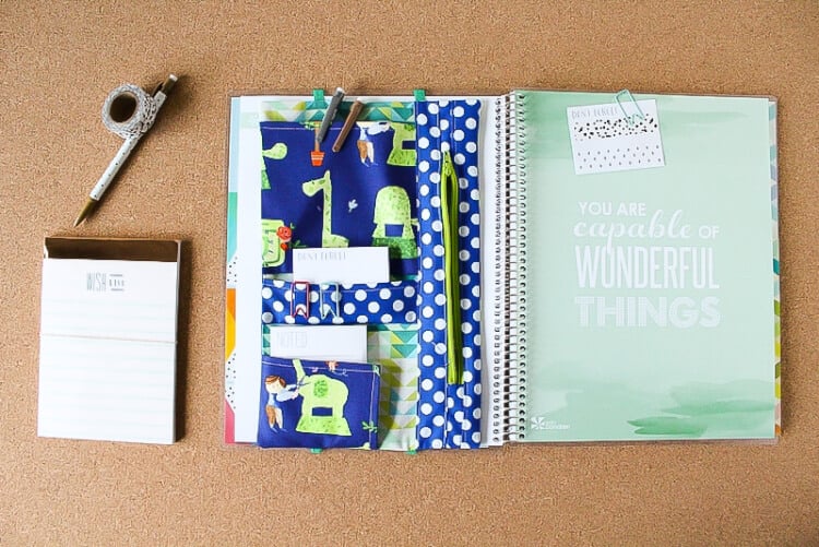 A pen, washi tape, note pads and pens by a fabric made planner organizer