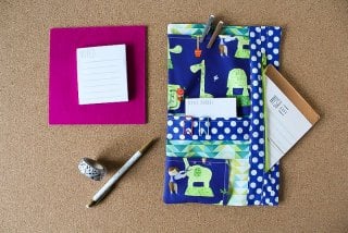 A pen, washi tape, note pads and pens by a fabric made planner organizer