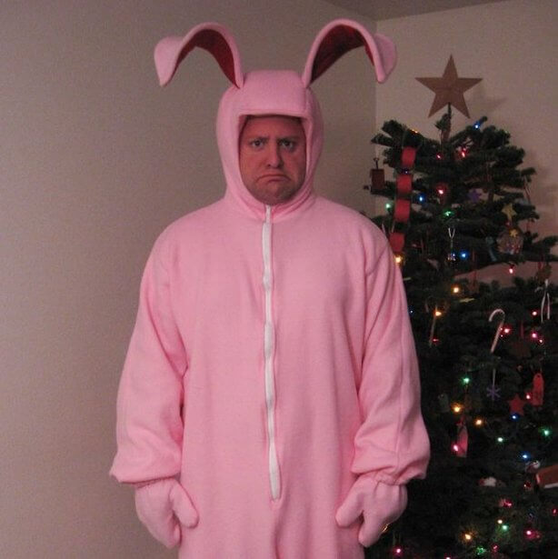 A man standing next to a Christmas tree, wearing a pink rabbit costume