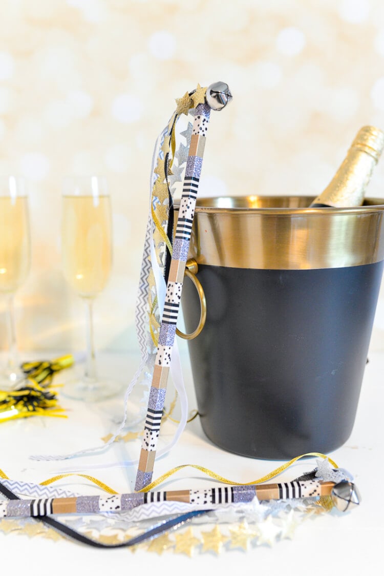 Two champagne flutes, a bottle of champagne in an ice bucket and two party streamers with bells on them, all sitting on a table