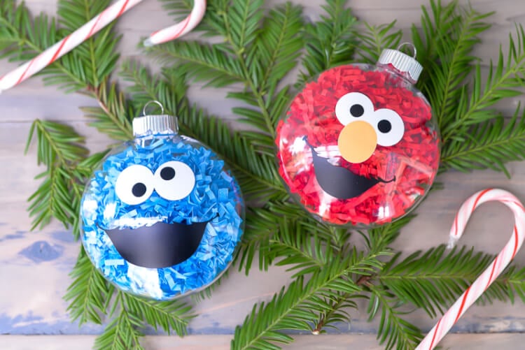 Some greenery, a candy cane and two glass ornaments decorated to look like Cookie Monster and Elmo from Sesame Street, all sitting on a table