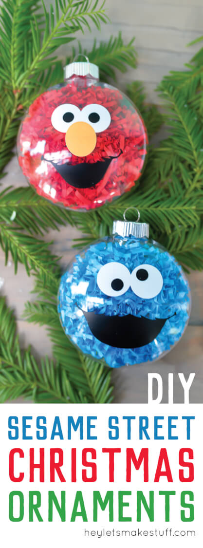 Some greenery and two glass ornaments decorated to look like Cookie Monster and Elmo from Sesame Street, all sitting on a table