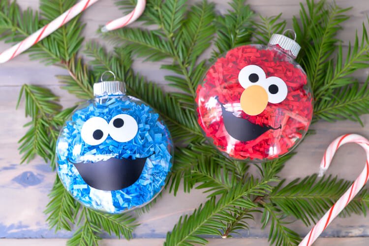 Some greenery, candy canes and two glass ornaments decorated to be Grover and Cookie Monster from Sesame Street all laying on a table