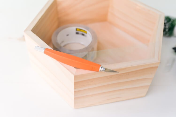 A wooden hexagon shaped shadow box with tape and a cutter