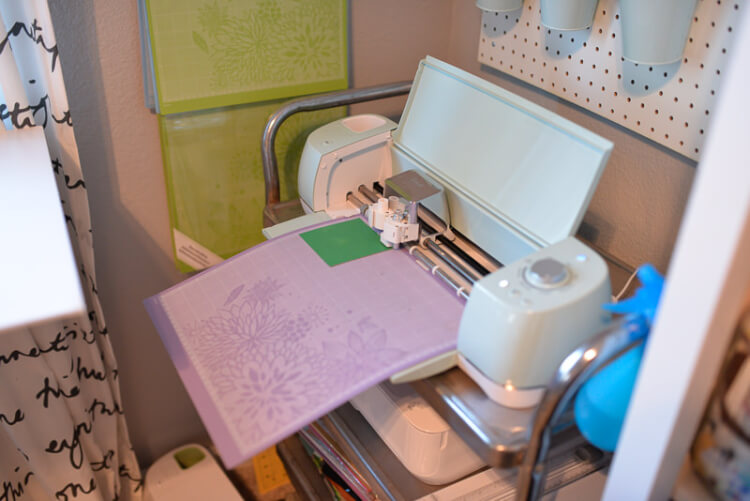 A Cricut machine sitting on a stand cutting a design from a purple mat
