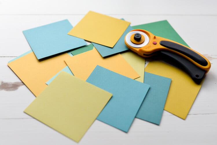 A rotary cutter and square pieces of cardstock laying on a table