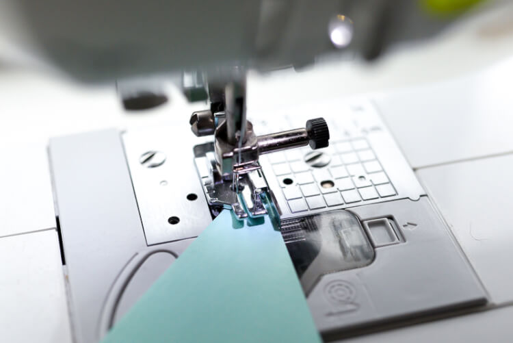 Image of a needle on a sewing machine with a piece of paper being sewn