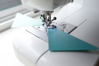 Image of a needle on a sewing machine with a piece of paper being sewn