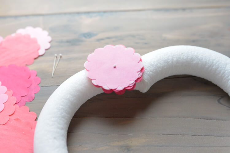 A heart-shaped foam wreath form, some straight pins, some tissue paper circles laying on a table and an assembled pile of tissue paper circles pinned to the wreath form