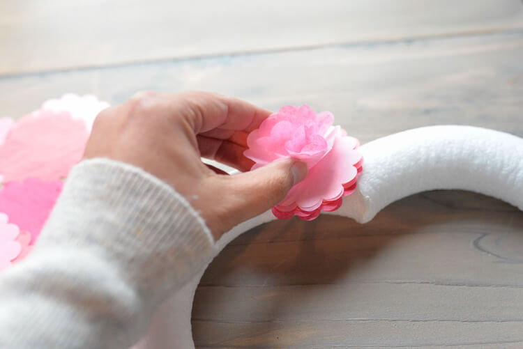 A woman\'s fingers fluffing up the tissue paper circles that are attached to the heart shaped wreath form