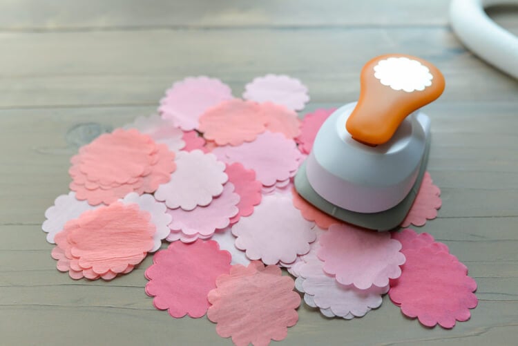 A scalloped-edge paper punch and tissue paper circles cut from the punch laying on a wooden table