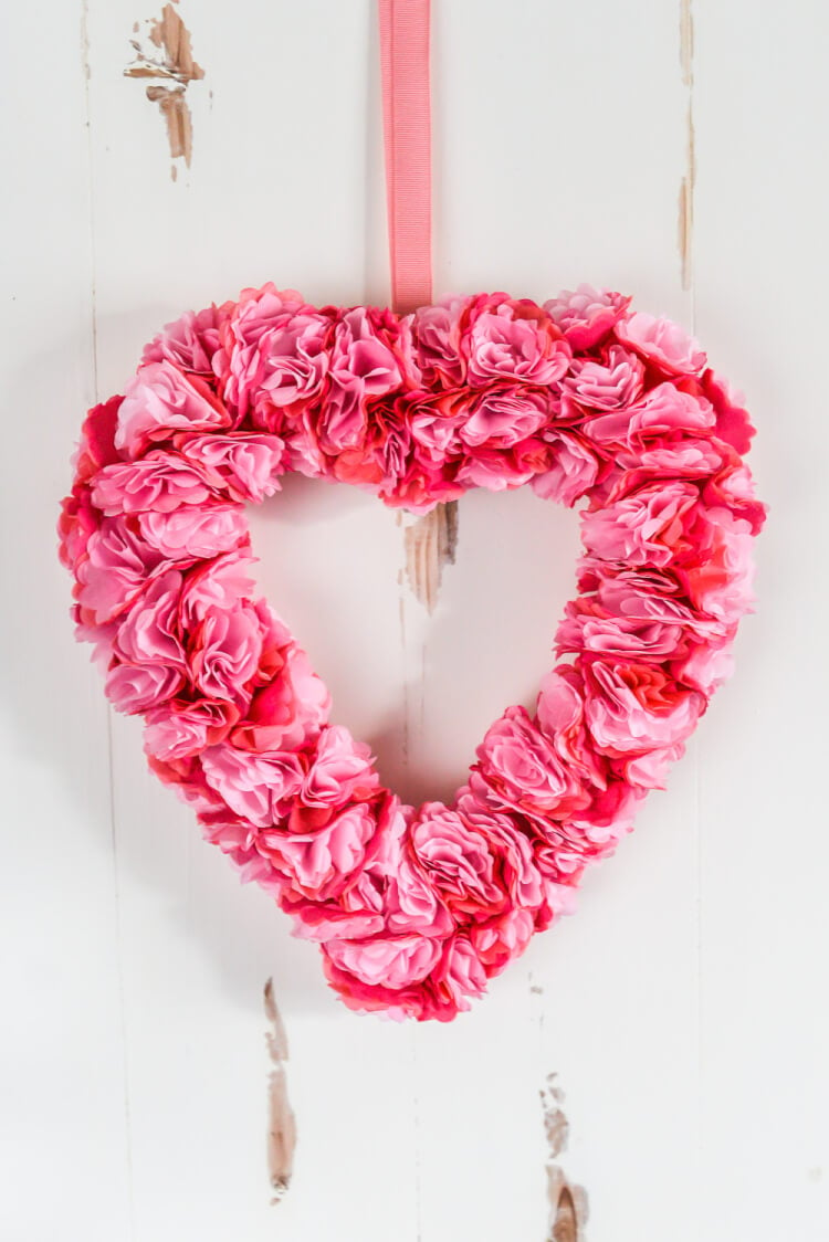 A close up of a heart shaped tissue paper flower wreath hanging from a door