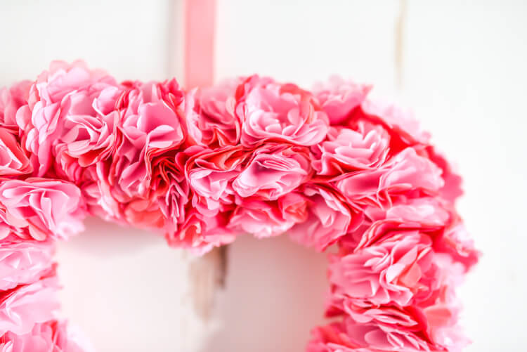 A close up of a heart shaped tissue paper flower wreath hanging from a door