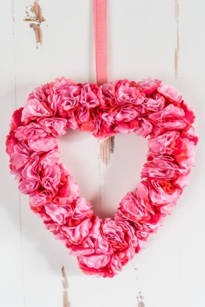 A heart shaped pink paper flower wreath hanging on a door