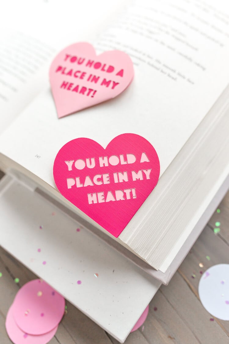 An open book lying on a table with a Valentine bookmark in the corner that says, \"You Hold a Place in my Heart!\"